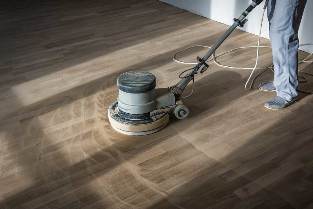 A close-up of vinyl plank flooring in a bright entryway with wet shoes and an umbrella placed on a doormat.